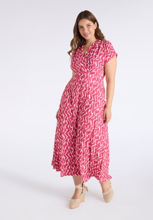 Vestido maxi en rosa con un patrón en zigzag, mangas cortas y diseño envolvente, combinado con sandalias de cuña tejidas. Tejido suave y ligero.