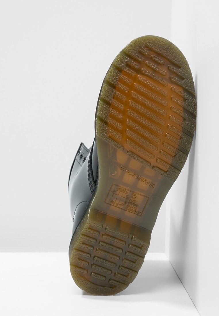 Semelle d'une botte noire avec une bande de roulement en caoutchouc brun translucide affichant un motif de grip texturé et un logo en relief.
