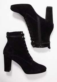 Botas de tobillo de ante negro con tacón alto, cordones en la parte delantera y cremallera lateral. Incluyen una textura suave y acentos de herrajes circulares.