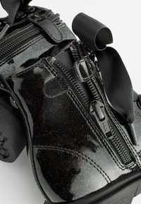 Scarpe con platform in pelle patent nera, caratterizzate da cerniere e larghe stringhe in raso, con una finitura scintillante e dettagli testurizzati.