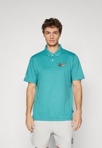 Turkis blå polo skjorte med krave og korte ærmer, med broderte detaljer på brystet og siden, laget av et mykt, teksturert stoff.