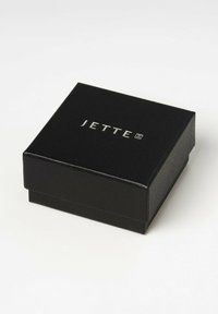Scatola per gioielli nera con finitura testurizzata. Presenta il logo in rilievo "JETTE" in argento sulla parte superiore. Forma quadrata, design compatto.