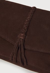 Braune Wildleder-Clutch mit einem geflochtenen Trageriemen und Quasten-Detail. Verfügt über eine glatte Textur und gestickte Kanten, die die Handwerkskunst hervorheben.