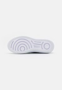 White sneaker sole with textured rubber grip, featuring circular patterns and lines. Smooth surface and a slightly raised edge.