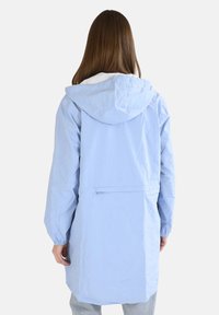 Veste à capuche bleu clair avec poignets élastiques et coupe ample. Matière lisse et légère avec un ourlet arrière plus long et un cordon ajustable.