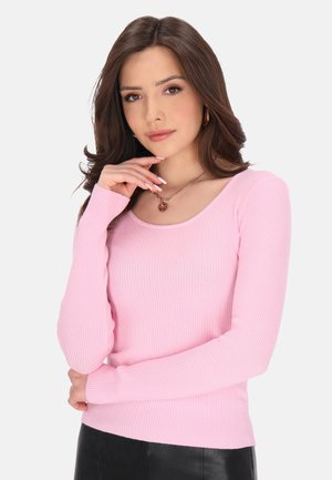 Top rosa a maniche lunghe con scollo a barca. Il tessuto ha una texture morbida. Abbinato a una gonna in pelle nera, che mette in risalto una silhouette aderente.