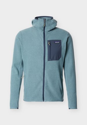 Gaiši zila teksturēta sporta jaka ar rāvējslēdzēju, kapuci un tumši zilu rāvējslēdzēju krūšu kabatā, Patagonia logotips uz kabatas.