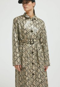Plašč z vzorcem kačje kože v bež in rjavih odtenkih, pasom, gumbi in ovratnikom. S sijajno površinsko obdelavo.