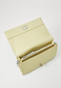 Yellow faux leather clutch with silver "CK" logo, magnetic closure, and zippered pocket inside. Smooth texture, minimalist design.