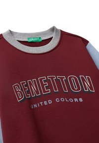 Vínová mikina s šedým žebrovaným límcem, světlomodrými rukávy a textem "BENETTON UNITED COLORS" na hrudi.