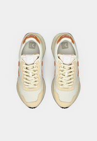 Beige og oransje joggesko med nettingoverdel, teksturerte detaljer, flate lisser, gummisåle og V-logo på tungen. Har et rent, moderne design.