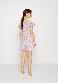 Vestido floral em tecido leve, com mangas curtas e fluidas e cintura ajustada, apresentando uma cor predominantemente roxa e um padrão floral vibrante.