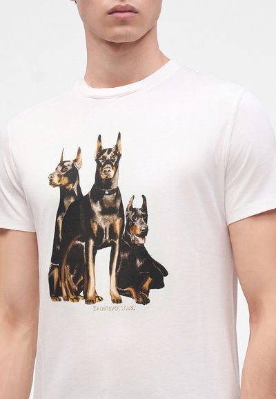 Λευκό t-shirt με λεπτομερή εκτύπωση τριών σκύλων Ντόμπερμαν, δύο όρθιων και ενός ξαπλωμένου, κεντραρισμένο στο στήθος.
