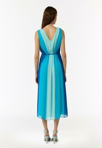 Ärmelloses V-Ausschnitt-Kleid mit einem Farbverlauf von hellblau zu dunkelblau. Der Taillenbund ist gerafft und wird mit hellblauen Absatzschuhen kombiniert.