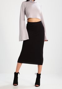 Grå kortärmad topp med hög krage, kombinerad med en svart figurnära midikjol. Modellen bär svarta ankelskor.