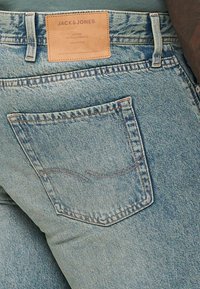 Jeans in denim azzurro chiaro con tasca posteriore caratterizzata da una sottile cucitura e un'etichetta in pelle beige che mostra "JACK & JONES."