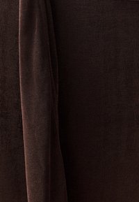 Bruine ribstof met een zachte textuur, voorzien van een gedrapeerd gedeelte dat het vloeiende ontwerp en de warme kleur benadrukt.