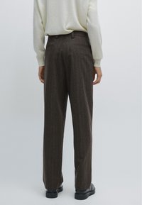 Bruna randiga byxor med rak snitt, tillverkade av textil med struktur, med midjeband och fickor, i kombination med en ljus tröja.