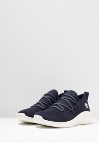 Baskets en maille marine avec lacets élastiques, semelles rembourrées et dessus texturé. Présentent un logo sur le côté et une languette de retenue pour un enfilage facile.