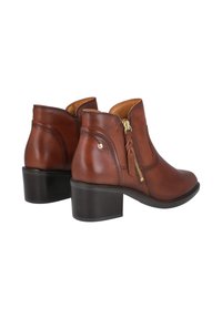 Botas de cuero marrón al tobillo con cremallera lateral, punta redonda y tacón apilado. Presenta un pequeño acento decorativo en el talón exterior.