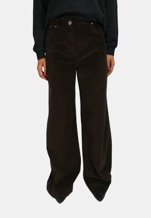 Pantaloni a gamba larga in corduroy marrone con tasche anteriori, chiusura con bottone e texture in corduroy visibile, indossati con un top nero e tacchi.