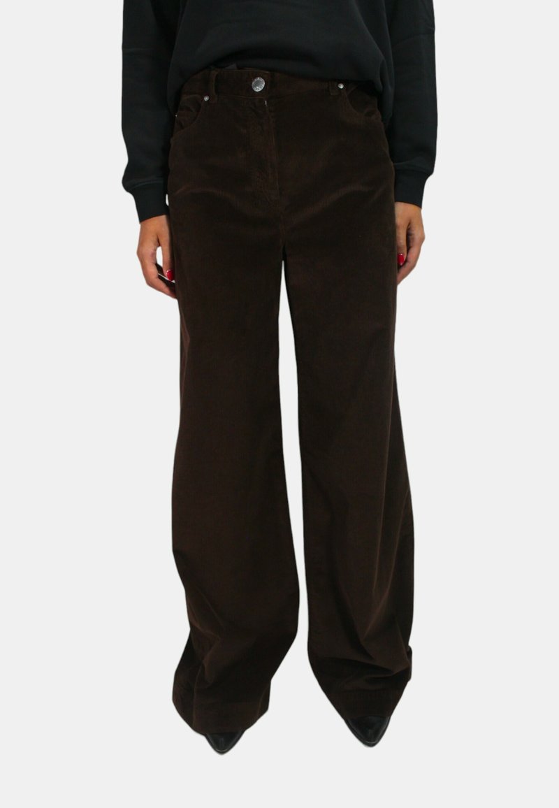 Pantaloni a gamba larga in corduroy marrone con tasche anteriori, chiusura con bottone e texture in corduroy visibile, indossati con un top nero e tacchi.