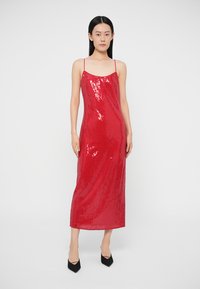 Sarkana spīdīgu fliteru kleita ar taisnu siluetu, plānām lencītēm un garumu līdz vidējai vēnā. Vienmērīga tekstūra ar visu kleitu klātām mirdzošām fliterēm.