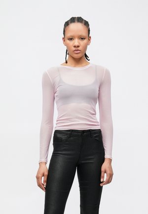 Przezroczysta, długorękawowa bluzka w jasnoróżowym kolorze, z okrągłym dekoltem, zestawiona z czarnymi, błyszczącymi, dopasowanymi jeansami. Gładka tekstura i dopasowany krój.