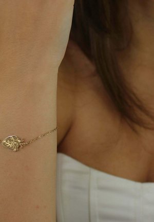 Bracelet en or avec un pendentif en forme de cœur orné de motifs détaillés de feuilles et d'animaux, attaché par une chaîne délicate. Texture lisse, finition brillante.