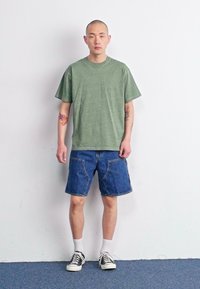 Grønn bomull t-skjorte med korte ermer, sammen med blå denim shorts. Svarte joggesko med hvite såler og ankel sokker fullfører looken.