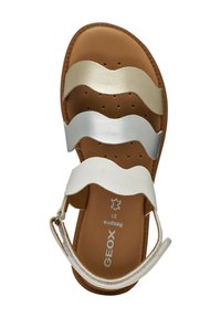 Sandalia plana de cuero marrón con tres tiras onduladas en blanco, plata y oro. Cuenta con una plantilla acolchada y hebilla ajustable en el tobillo.