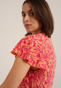 Short-sleeve dress in a pink and orange floral pattern, featuring a textured fabric and ruffled sleeves with open side detail.