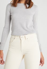 Jasnoszary sweter z długim rękawem i okrągłym dekoltem, zestawiony z białawymi dżinsami o wysokim stanie, wyposażonymi w zapięcie na guziki i klasyczny fason z pięcioma kieszeniami.