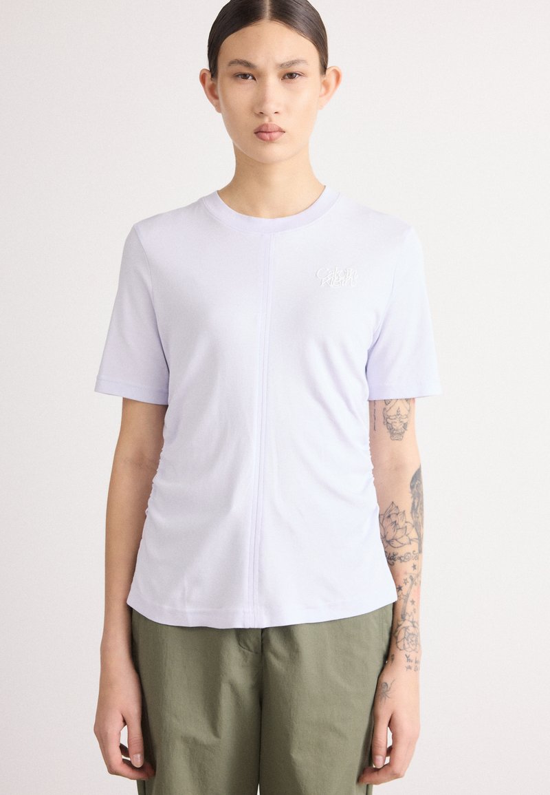 Lila, rövid ujjú póló puha anyagból, diszkrét Calvin Klein logóval, kerek nyakkivágással és gyűrt oldali részletekkel.