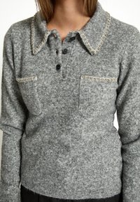 Pullover grigio in maglia con scollo a colletto, caratterizzato da decorazioni sul colletto e sulle tasche, e tre bottoni neri sul davanti.