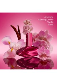 Rosa Calvin Klein Parfümflasche, umgeben von pinkfarbenen Orchideen, Vanilleschoten und weißen Blumen auf einer reflektierenden Oberfläche mit aufgeführten Duftnoten.