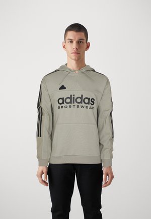 Sudadera gris claro con el logotipo negro de "adidas", capucha con cordón y franjas negras contrastantes en las mangas. Incluye un bolsillo frontal tipo canguro.
