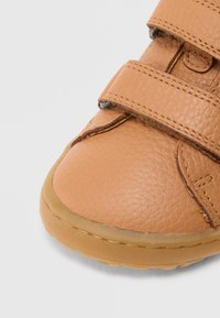 Παπούτσι από ταμπά δέρμα με στρογγυλεμένη μύτη, δύο λουράκια με βέλκρο και υφασμένο πάνω μέρος με ορατές ραφές· διαφανής ελαστική σόλα.