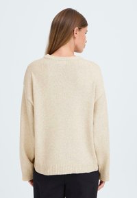 Pull en tricot beige à col rond, épaules tombantes et ourlet côtelé. Texture douce, coupe décontractée et design légèrement surdimensionné.