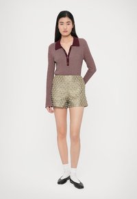 Geribd bordeaux rood langermig shirt met een kraag met twee knopen, gecombineerd met glanzende olijfgroene shorts met een getextureerd ruitpatroon.