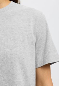 Sivé bavlnené tričko s okrúhlym výstrihom, krátkymi rukávmi a mäkkou textúrou. Má čisté švy a jednoduchý dizajn bez ozdôb.
