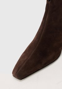 Bottine en daim marron avec un bout pointu et une silhouette élancée. Présente une texture lisse et un design minimal sans matériel visible.