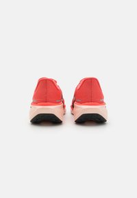 Chaussures de sport en corail vif avec un dessus en maille texturée, semelle intermédiaire rembourrée et semelle en caoutchouc noir. La vue arrière montre la hauteur et la forme.
