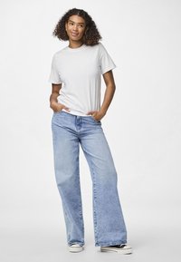 Hvit bomull t-skjorte, avslappet passform, parret med lyseblå vide denimjeans og svarte lave sneakers. Glatt tekstur, klassisk design.