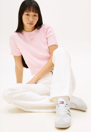 Pull léger en tricot côtelé rose clair à manches courtes, jean large blanc, et baskets blanches avec des rayures vertes et des accents colorés.