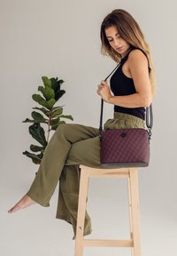 Bordeauxfarbene, gemusterte Umhängetasche mit strukturiertem Oberflächen, schwarzen Hardware-Elementen und verstellbarem Riemen, kombiniert mit olivgrünen, weit geschnittenen Hosen.