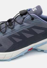 Blue and gray trail running shoe with a textured upper, lace lock system, and a durable sole featuring a contrasting white midsole.