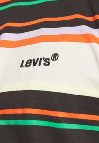 Logo Levi's brodé sur un tissu rayé multicolore avec des bandes horizontales vertes, orange, blanches, noires et marron.