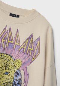 Sudadera color crema con un gran gráfico impreso de leopardo, con acentos en púrpura y amarillo y un diseño texturizado.