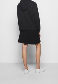 Černá mikina s kapucí a přední kapsou, s asymetrickým lemem, doplněná černou flitrovou sukní. Oblečení doplňují bílé tenisky.